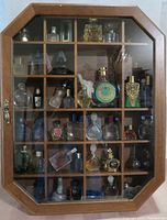 Front view of wooden octagonal display cabinet filled with multiple-perfume bottles on shelves.