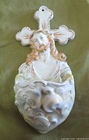 Front view of a ceramic holy water font featuring a detailed relief of Jesus and an attached cross with gold accents.