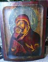 Full view of the wooden religious icon showing Virgin Mary holding baby Jesus, aged paint with visible patina and gold detailing on the halos