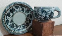Blue ceramic cup and saucer with intricate floral and vine designs in shades of blue.