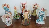 Group photo of seven Boyd's angel figurines with translucent textured wings and colorful floral details, displayed in a row on wood surface.