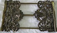 Close-up top-down view of one ornate extendable metal book holder showing intricate cutout floral and scroll designs in brass-colored metal.