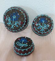 Three small round baskets with dark fabric and intricate bead floral embroidery in blue, teal and red colors