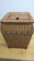 Front view of antique sewing/knitting basket made of woven wicker with decorative horizontal bands, wooden knob on top compartment.