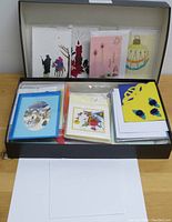 Photo showing an open box containing a collection of pre-made greeting cards with diverse colorful holiday and decorative designs.