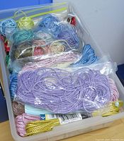 A tub containing thick metallic threads in clear bags in colors like lavender, blue, green, gold, pink, and silver for crafting use.