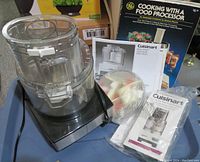 Food processor base with clear work bowl and locking lid on top. Accessories and manuals alongside.