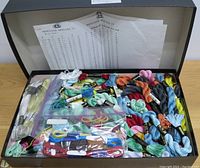 Open black box showing a large quantity of varied-color Mouline Special 25 embroidery floss skeins with printed charts inside the box lid.