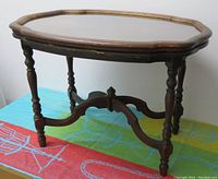 Side view of wooden side table with scalloped edges and turned legs on colorful fabric background.
