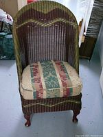 Front view of the Lloyd Loom Broad chair showing the woven wicker, cushion with multi-color damask striped upholstery, and wooden legs.