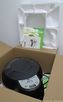 Photo showing black and gray Tfal Actifry air fryer in open cardboard box with white styrofoam packaging and user manual inside.
