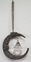 Hanging crescent moon ornament made of pewter with a crystal inside it, shown against a white wall.