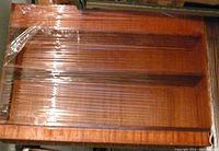 Full view of the two-tier wooden plant shelf wrapped in plastic, showing the rectangular shape and two deep shelves with an upper cut-out area for the aluminum trough.