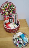 Vintage woven sewing basket with floral fabric lining containing various sewing notions and a plastic container with assorted buttons and snaps.