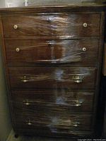 Front view of wooden six-drawer highboy dresser shrink wrapped, showing the different drawer knobs and pulls.