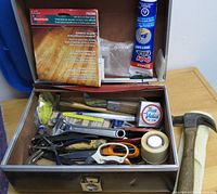 Photo of metal toolbox open with assorted hand tools including hammer, wrench, scissors, tape, and others inside