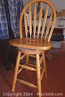 Front and side views of a light wood bar stool with curved backrest slats, round swivel seat, and turned legs with footrest.