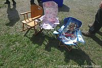 Photo showing all three children's chairs outdoors on grass: one wooden rocking chair and two folding fabric chairs