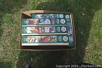 Top view of five boxed Cobbler 1000-piece jigsaw puzzles arranged side by side in a cardboard box on grass.