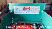 Green Coleman Easi-Lite camping stove with label and control instructions on the inside lid panel.