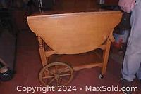 Side view of maple tea wagon showing drop leaf sides, large wooden spoked wheels and caster wheels, and turned supports.