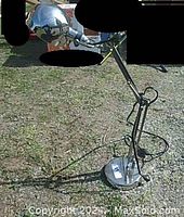 Chrome adjustable desk lamp standing outside on grass, showing full lamp structure with flexible arms, round chrome base, and spherical lamp head.
