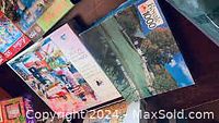Photo showing four 1000-piece jigsaw puzzles stacked on a table. Images include cityscape, coastline, and countryside scenes.