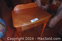 Front view of maple wooden table showing smooth tabletop, drawer with metal knob, and curved backsplash.