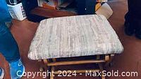 Photo showing the cushioned top of the rocking ottoman with gray patterned fabric upholstery.