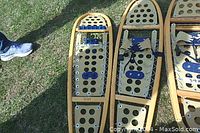 Two wooden snow shoes side by side, showing beige perforated decking and wooden frames, laid on grass outdoors.