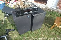 Sony FM/AM stereo receiver amplifier on top of two Pioneer speakers outdoors with speaker wires on top.