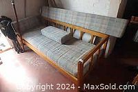 View of the wooden Chesterfield sofa with visible wooden slat frame and plaid upholstery cushions, two cushions on seat and back, one cushion is rolled lumbar support pillow.