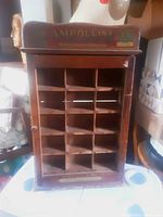 Front view of wooden display cabinet with 15 cubby compartments and vintage advertising on the top backboard.