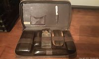 Full open view of the antique leather travel case showing organized storage of grooming and toiletry containers and brushes secured with straps.