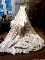 Full length view of the satin wedding gown showing long train spread on floor and dress form in background.