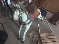 View of the heavier antique wooden rocking horse painted light green with black mane and tail, leather saddle, and detached rocking base on the floor next to it.
