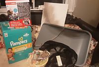 Photo showing silicone changing mat on a chair, unopened box of Pampers Swaddlers diapers size 2, black stroller bunting and bottle sterilizer box.