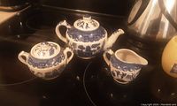 All three items: teapot with lid, sugar bowl with lid, and creamer arranged on stovetop, showing size and overall condition with Blue Willow blue pattern on white porcelain.