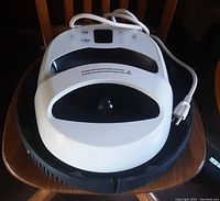 Top view of a white digital heat press machine showing black handle and digital display control panel with temperature and timer buttons, along with attached power cord.