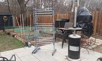 Full view of the large clothes drying rack standing on a patio with garden and furniture background.