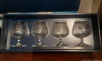 Box display showing 4 different etched design wine glasses arranged in a row inside a single box.
