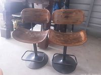 Front view of two reclaimed wood bar stools with black metal bases and footrests.