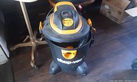 Full view of the Shop-Vac wet/dry vacuum showing black body with yellow accents on wheels, handle, and hose holder.