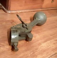 Vintage heavy cast iron train bell clanger lying on wooden floor showing clamp and screw mounting mechanism.