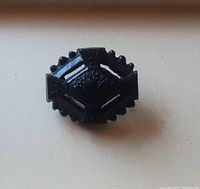 Front view of black carved jet brooch with decorative motifs and scalloped edges.