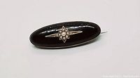 Front view of the brooch showing elongated oval black enamel surface with star-shaped seed pearl design.