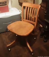 Full view of the wooden office chair showing wood seat and backrest, castor wheels, and base structure.