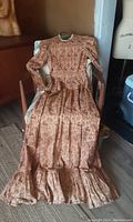 Full view of vintage prairie dress laid out on chair, showing full length and ruffled hem.