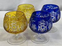 Four Ajka Marsala cut to clear brandy snifters in cobalt blue and amber with cut floral and geometric pattern, showing overall lot and colors.