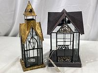 Pair of architectural style glass and metal candle lanterns, side by side on white background.